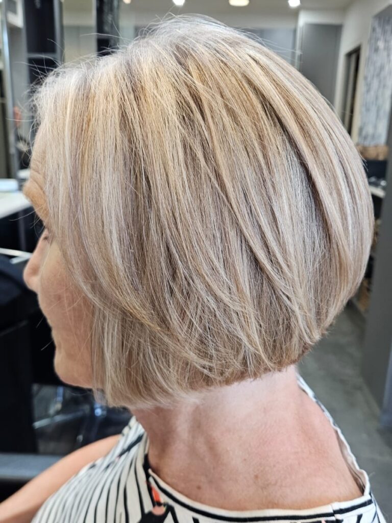 A side profile of a woman showcasing a rounded chin length sandy blonde bob haircut with subtle layers.