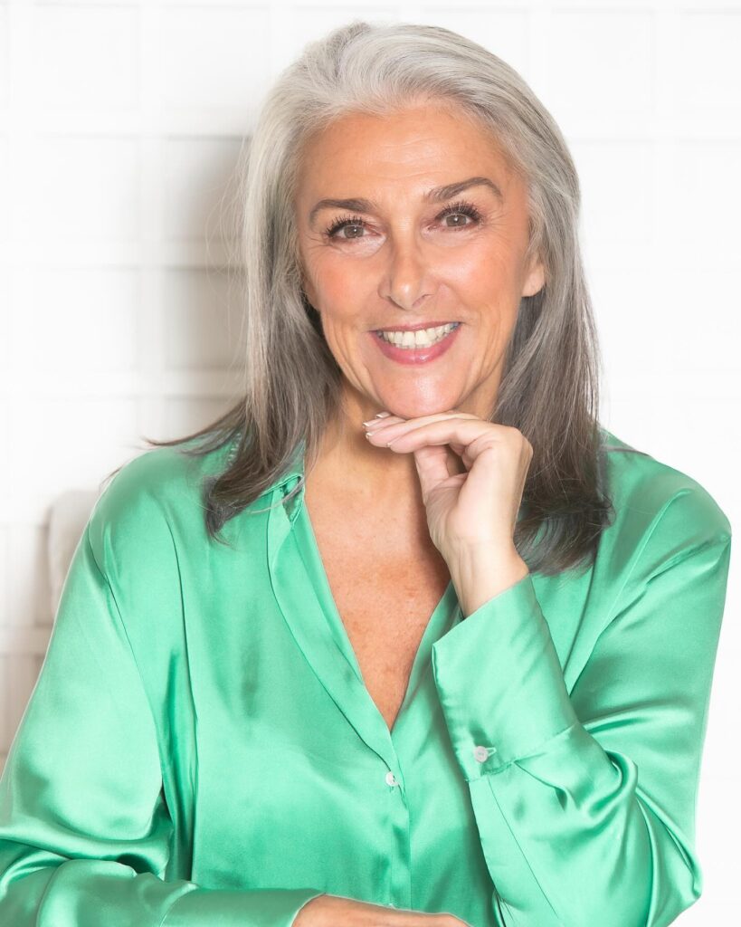 A smiling woman with long silver and grey hair styled in a swept back layered look.