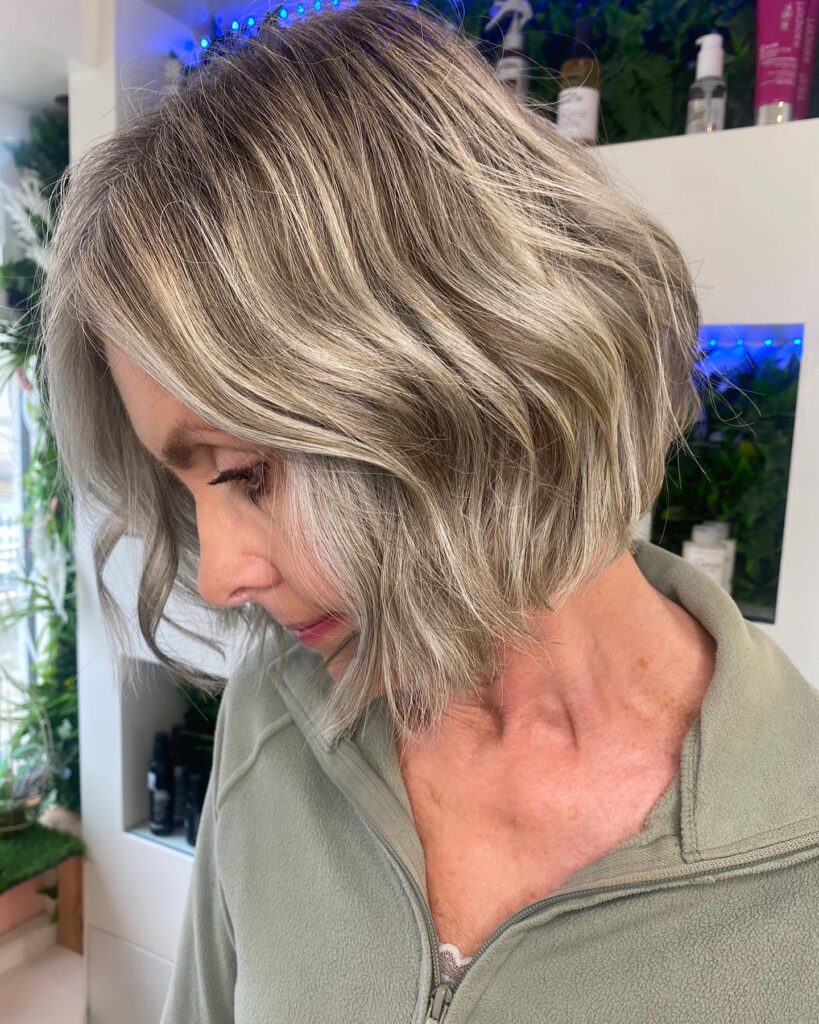 A woman showing a side profile of a chin length ashy mushroom blonde bob with soft waves.