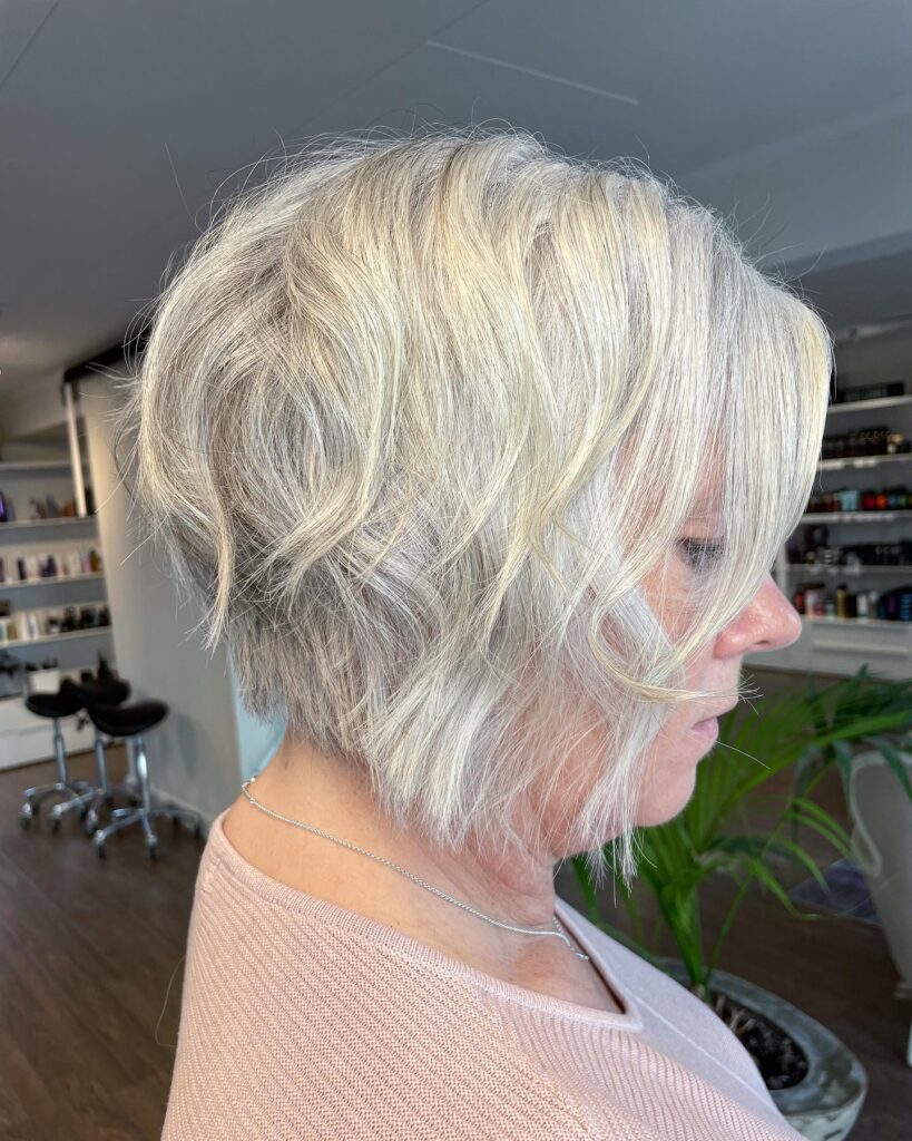 A woman showing a side profile of an icy platinum angled wavy bob with textured layers.