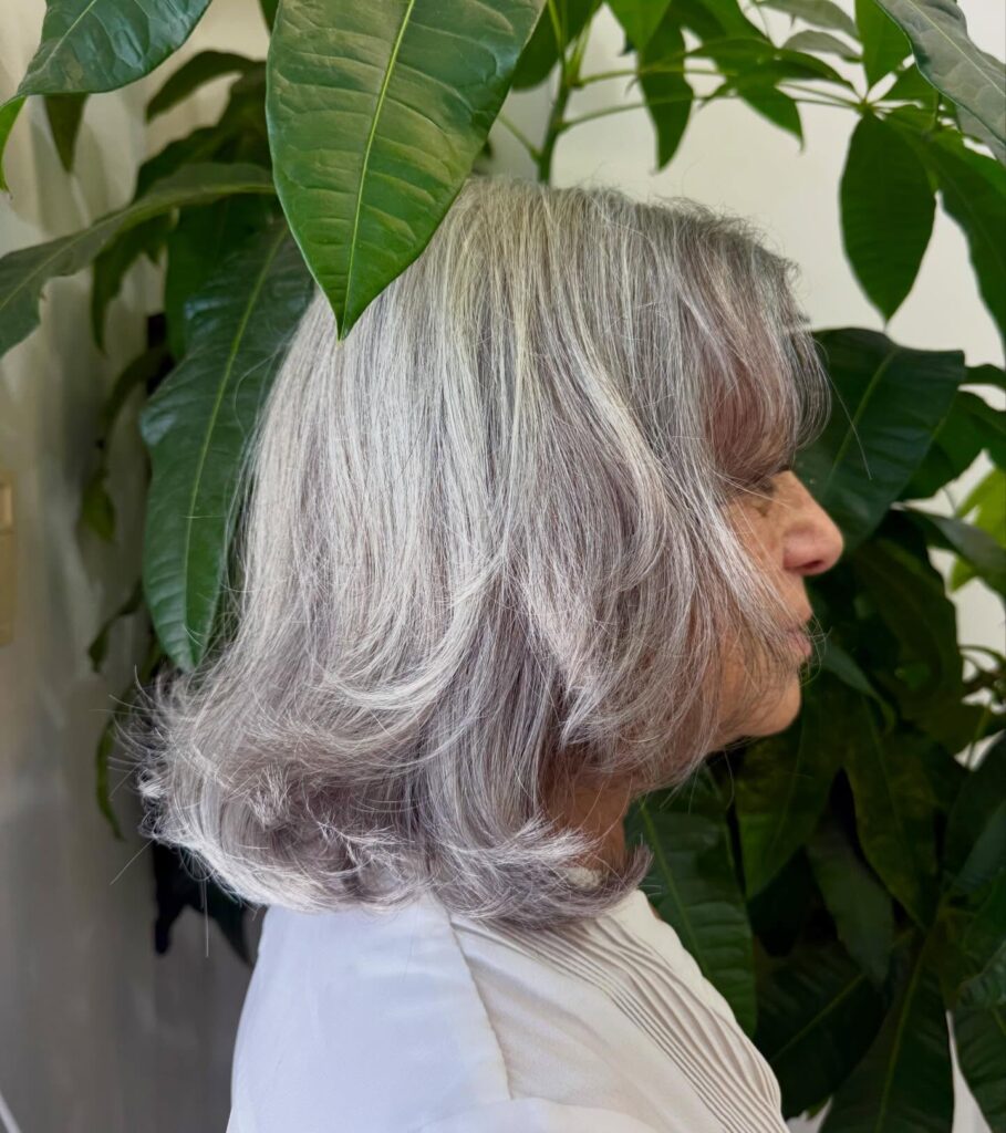 A side profile of a woman with a shoulder-length silver lob haircut featuring soft face-framing layers and flipped ends.