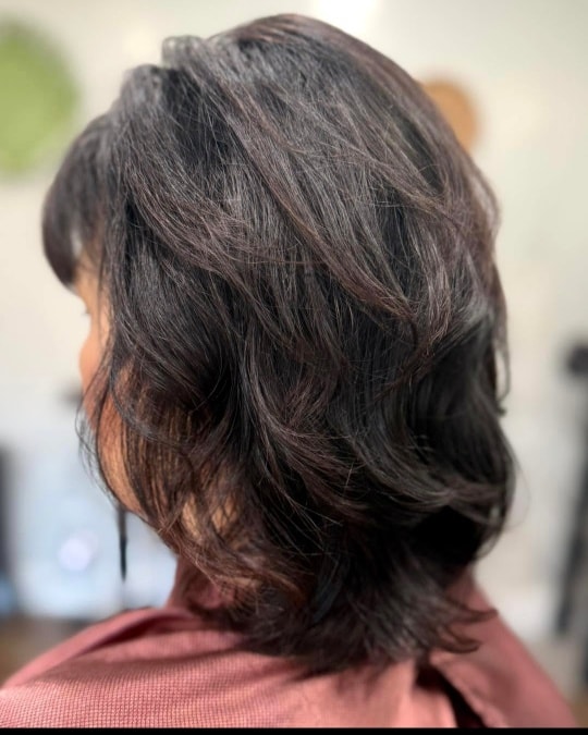 A side profile view of a woman showcasing a shoulder-length platinum blonde lob haircut with wispy face-framing layers that flip outward at the ends.