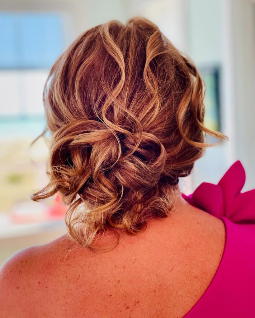 A back view of a woman with caramel blonde hair styled in a loose romantic low chignon with twisted curls.