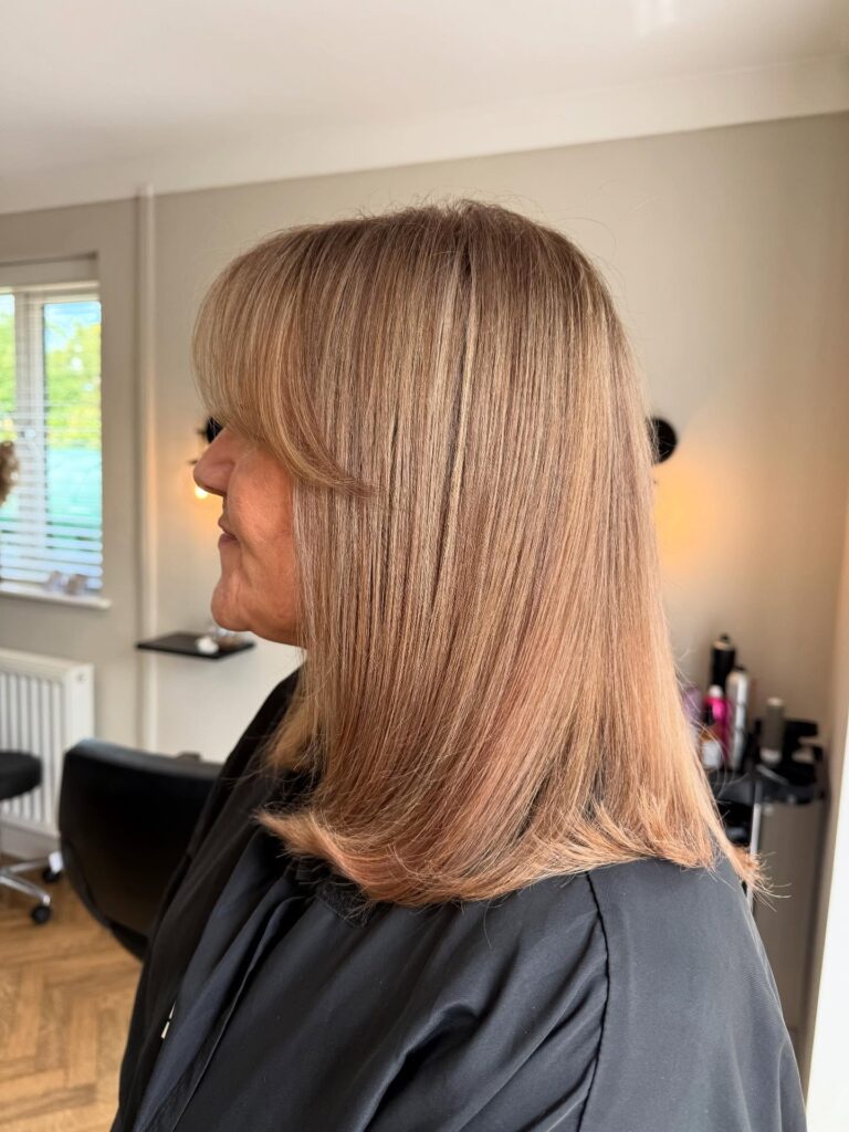 A side view of a woman with a sleek strawberry blonde shoulder length haircut and soft face framing curtain bangs.