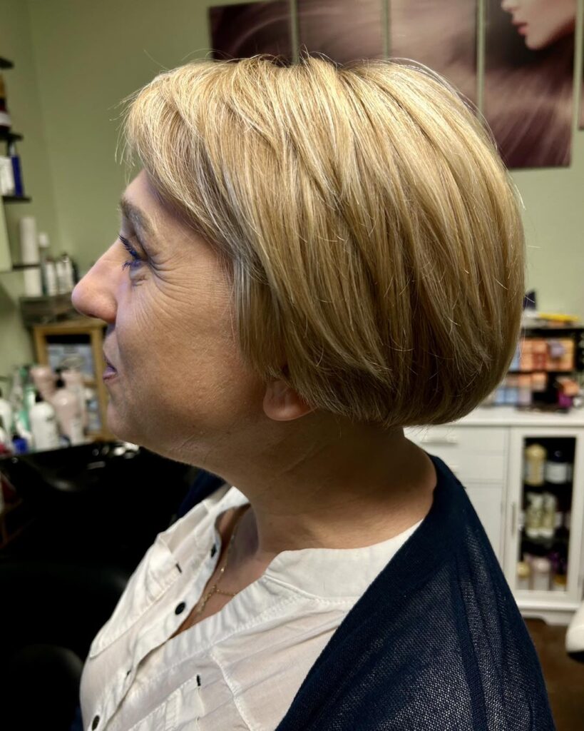 A woman from a side profile view displays a rounded ear-length graduated bob with soft crown layers and dimensional honey blonde tones.