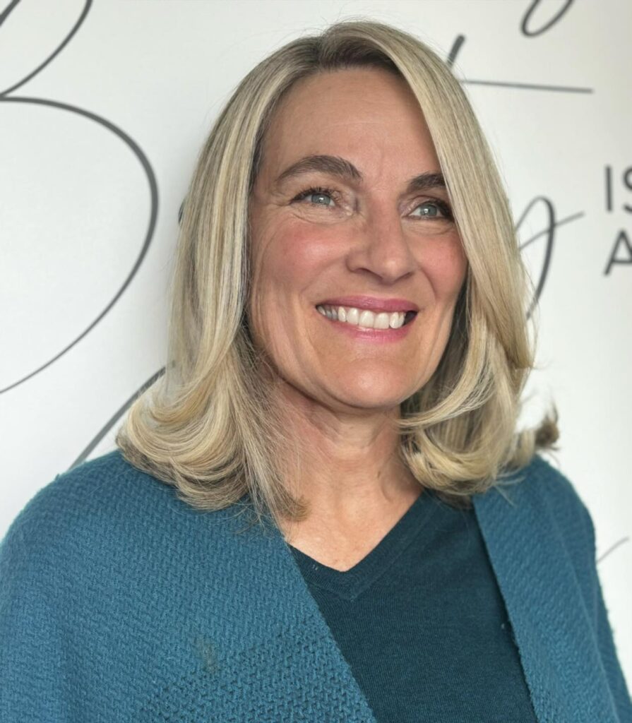 A smiling older woman with green eyes showcases a shoulder-length ash blonde lob with a side part and softly flipped-out ends.