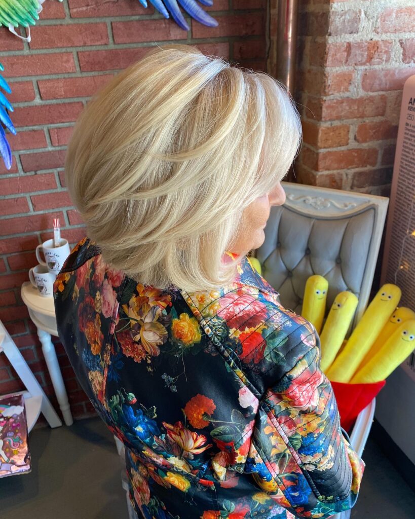 A woman from a back-angle view displays a textured jaw-length stacked bob haircut with dimensional bright blonde balayage highlights.