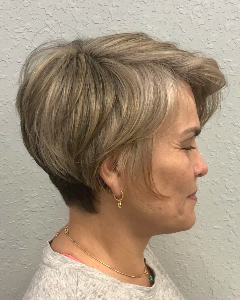 A woman with fine hair shows off a structured ash blonde pixie cut with long textured crown layers and a side-swept fringe.