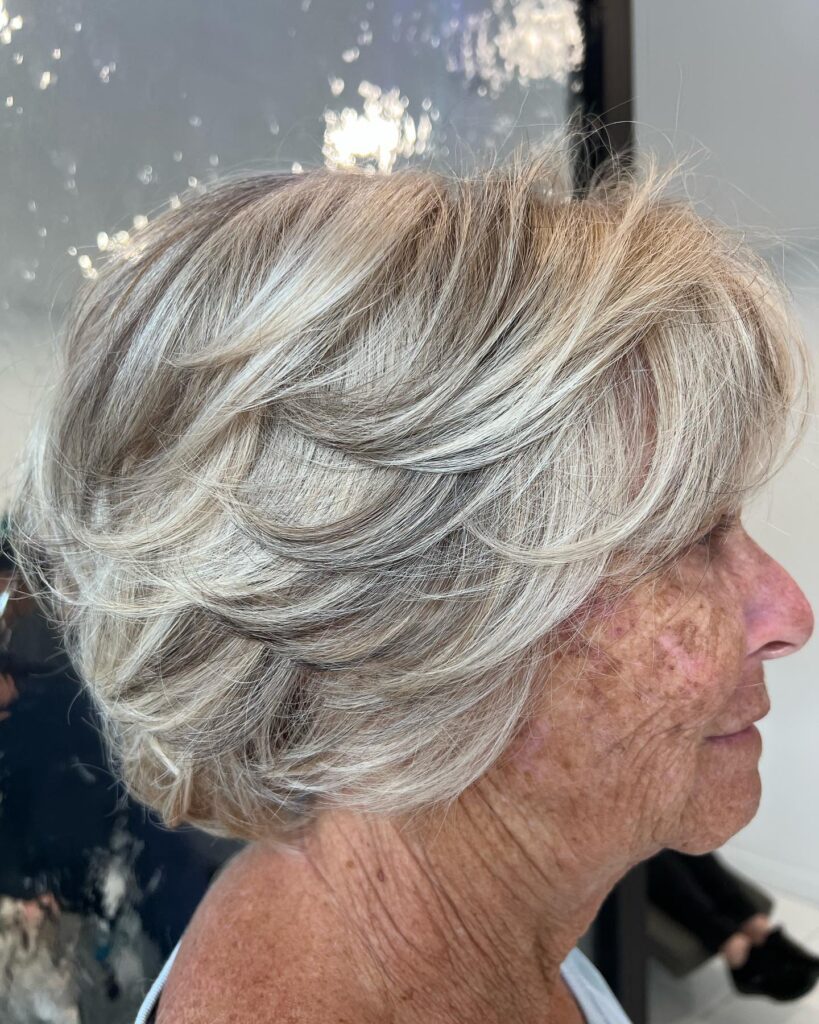 A side profile photograph of a woman with a short, textured icy white pixie wedge haircut featuring choppy layers on top.