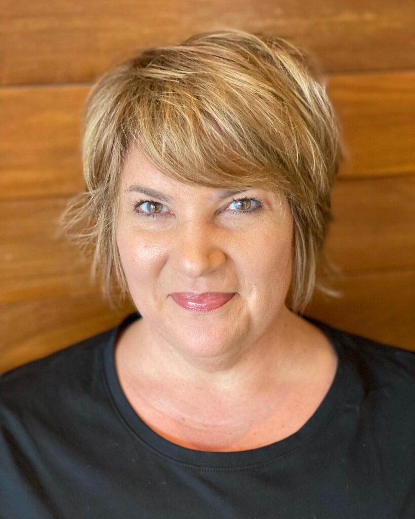 A side profile photograph of a woman over 60 showcasing a straight, angled silver blonde bob haircut with a polished rounded shape.