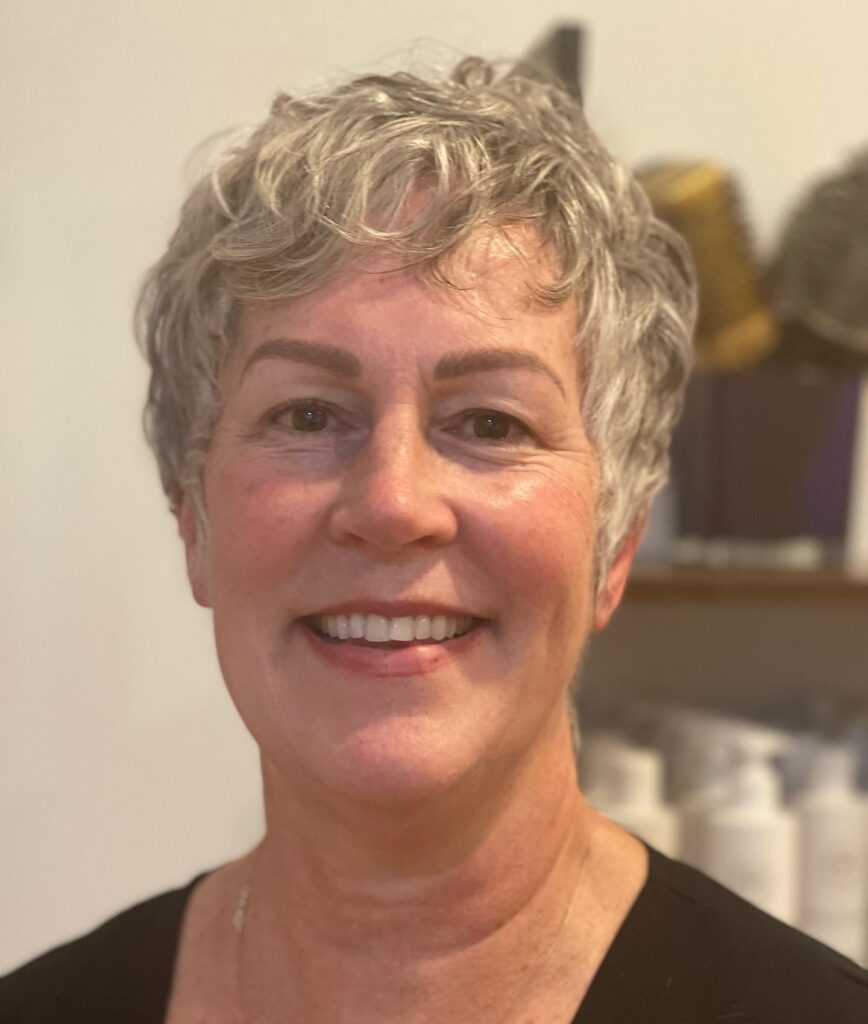 A woman over 60 with a short layered wavy silver pixie cut smiling for a portrait.