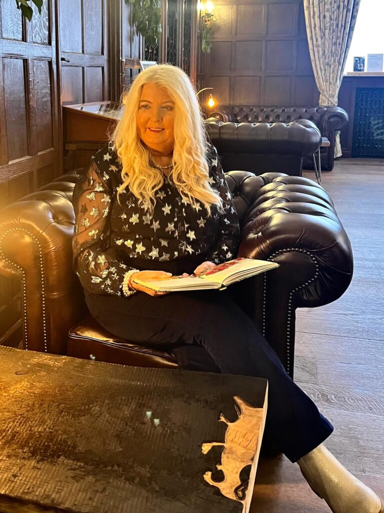 A woman over 60 sitting in a leather chair with very long platinum blonde hair styled in loose beachy waves.