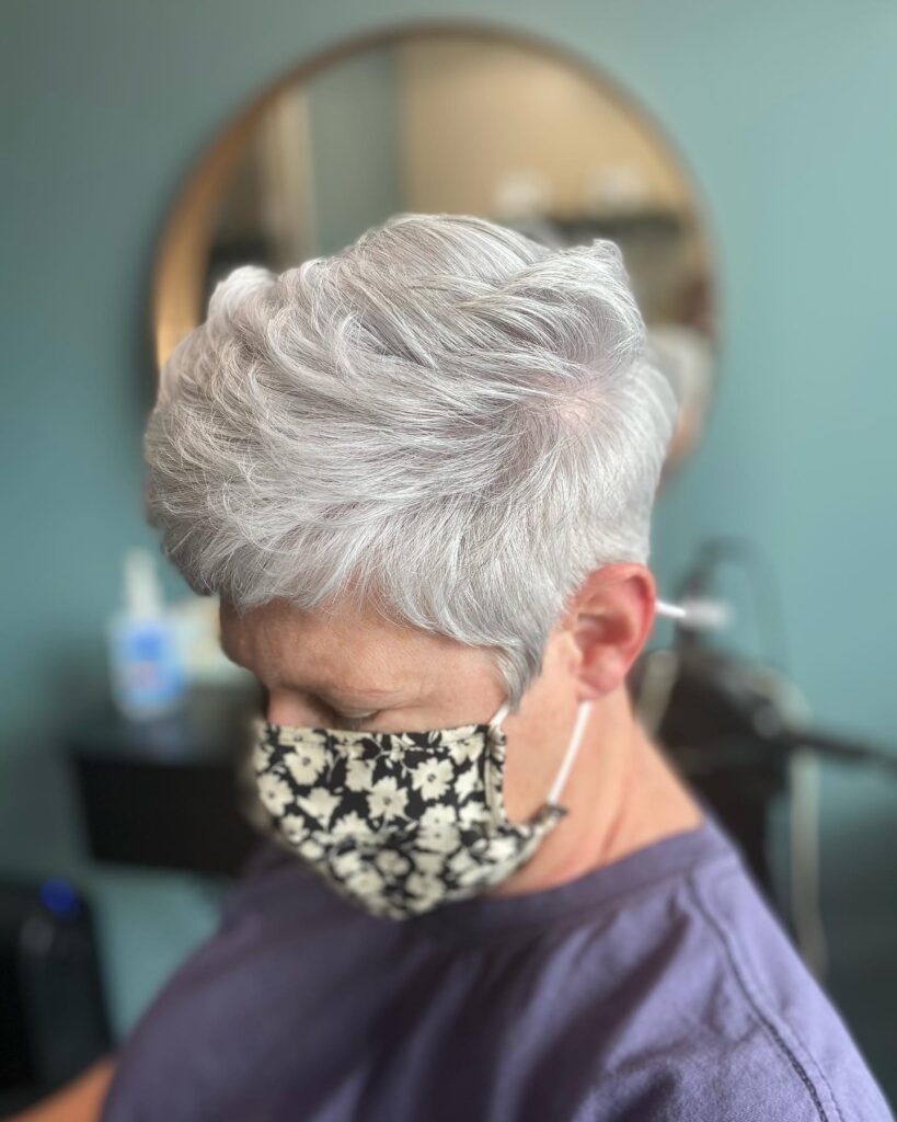 A woman with a short tapered silver pixie cut that has wavy texture and volume on top.