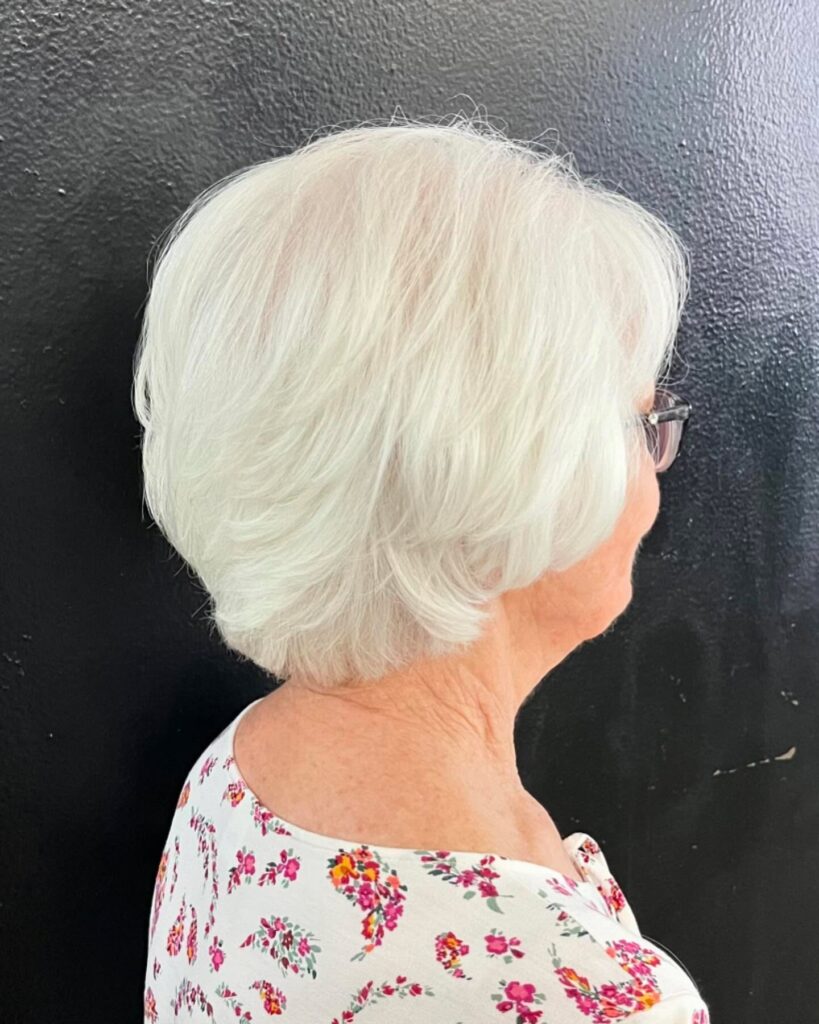 The side profile of a woman with a feathery, pure white layered bob haircut styled with a soft backward sweep.