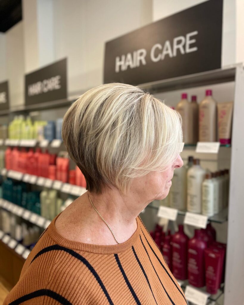 The side profile of a woman with a feathered soft silver pixie bob haircut featuring light layers swept back from the face.