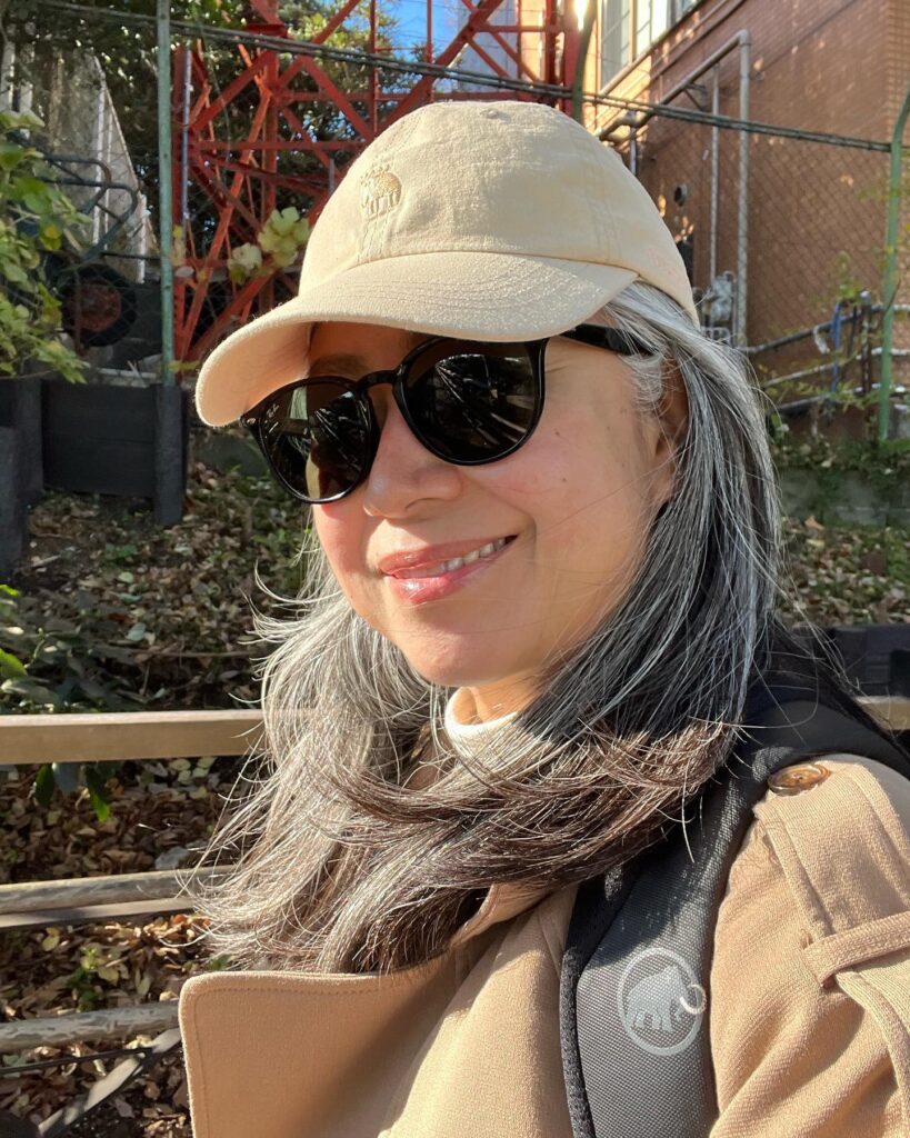 A woman over 60 looking downward to show the top profile of a textured dark brunette pixie haircut with wispy asymmetrical bangs.