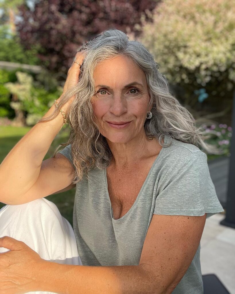 A smiling woman over 60 with a voluminous neck-length silver shag hairstyle featuring textured layers and curtain bangs.