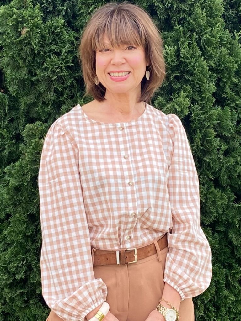 A woman with a straight, graduated inverted bob haircut with blonde highlights wearing a black jacket and a gold necklace.