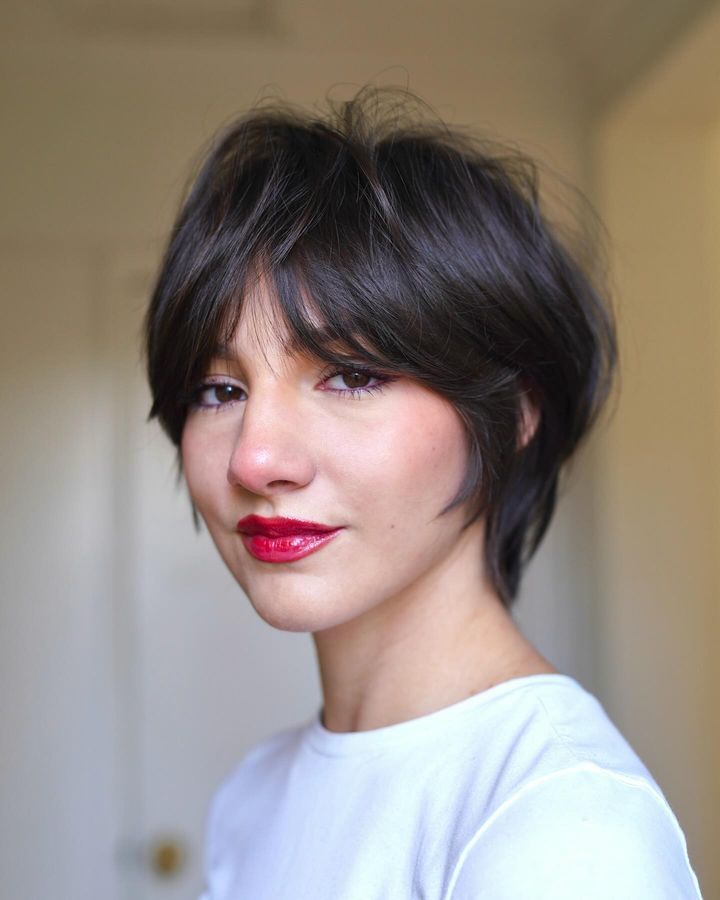 A woman with a short layered and textured dark brunette shaggy pixie bob haircut with sweeping bangs.