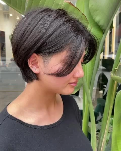 Side profile view of a woman with a dark charcoal tapered pixie bob and sweeping side bangs.