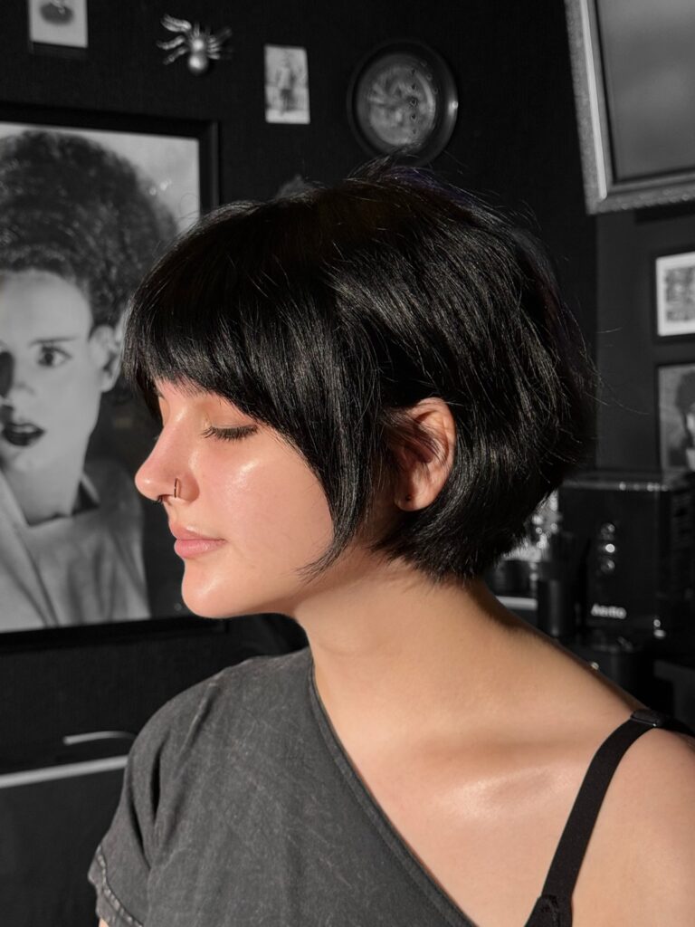 Side profile view of a woman showing off a shiny jet black short French bob with full brow grazing bangs.