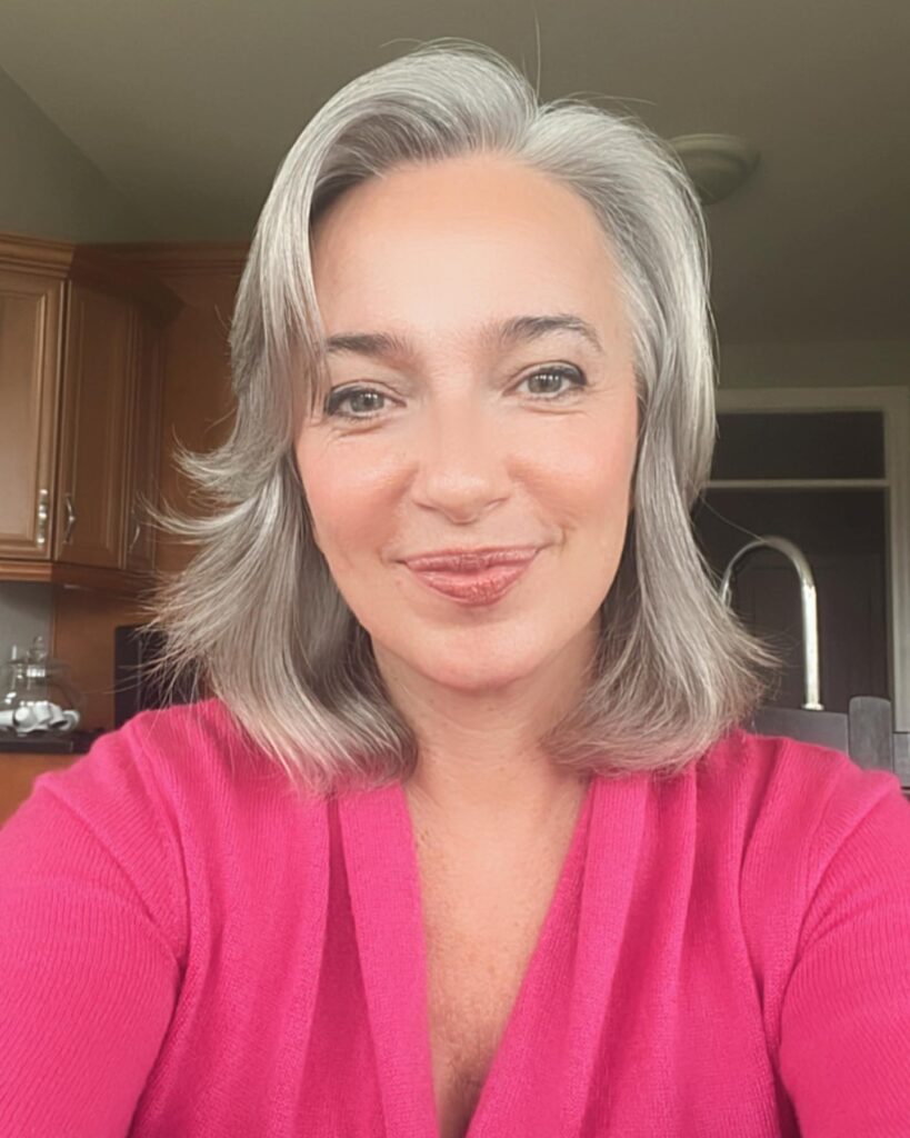 A woman with a silver shoulder length lob haircut featuring face framing feathered layers.
