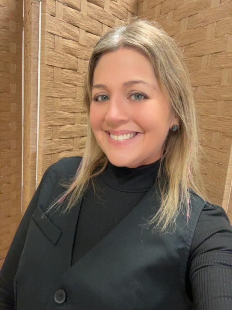 A woman with medium length layered blonde hair smiling with a center part.