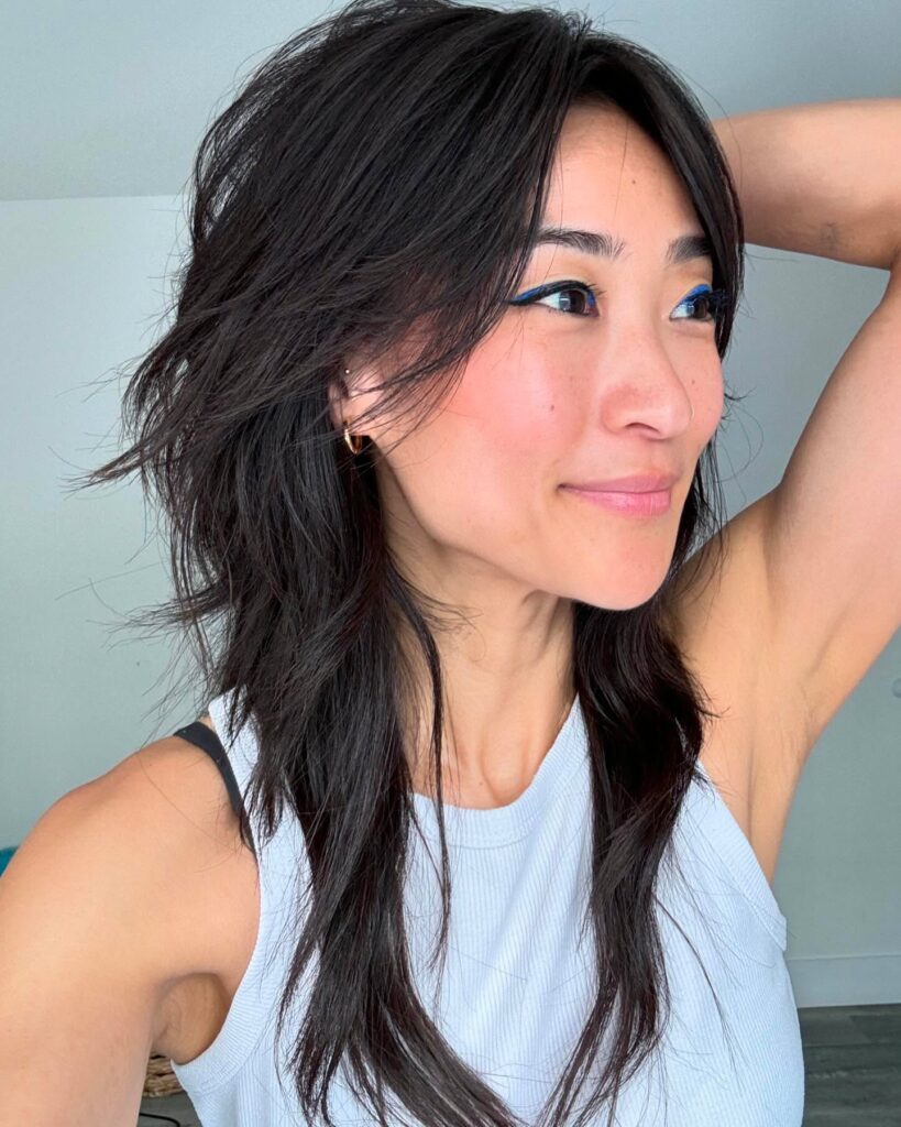 A woman with long textured dark brown hair cut in a heavily layered shag with curtain bangs.