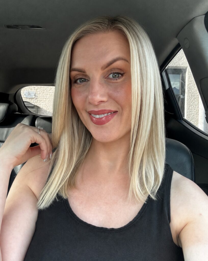 A smiling woman with a sleek straight bright blonde shoulder length lob haircut parted down the middle.