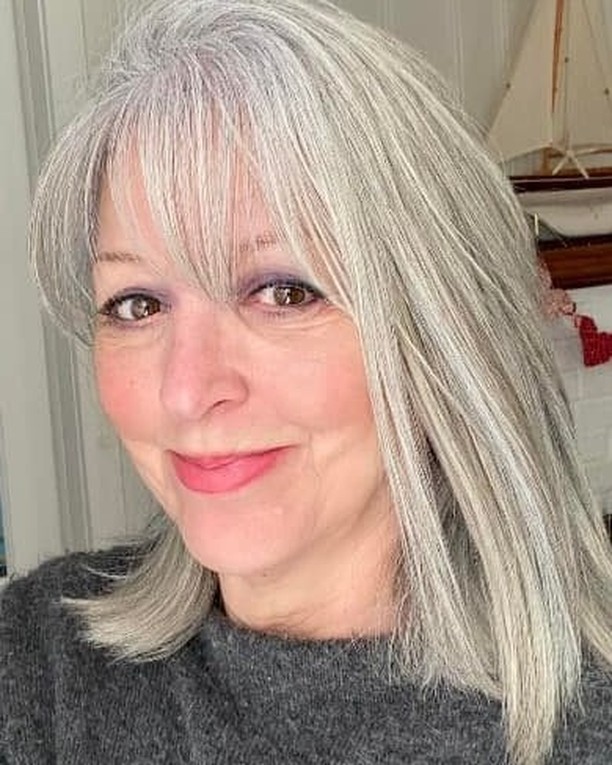 A woman with a straight, silver, shoulder-length lob and light, feathery bangs.