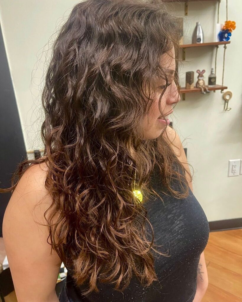 A side profile view of a woman with a long brunette choppy bob hairstyle featuring messy natural waves and face-framing layers.
