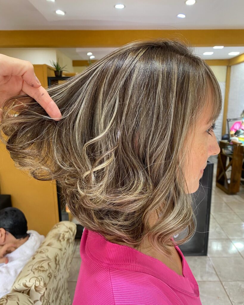 A side profile view of a woman with a shoulder-length brunette bob featuring voluminous blonde balayage curls at the ends.