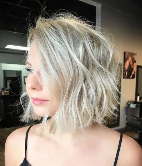 A side view of a woman showcasing a neck-length choppy platinum blonde bob with messy textured waves.