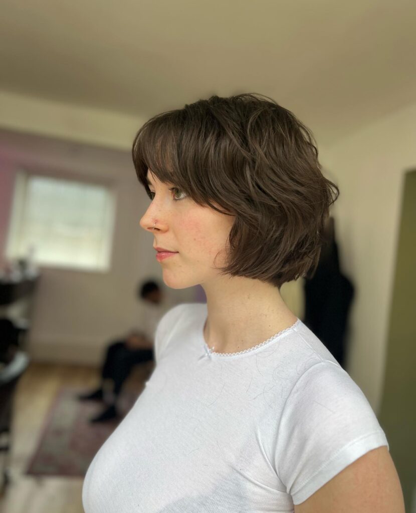 A side profile view shows a woman with a dark chocolate brunette French bob styled in messy, textured waves with curtain bangs.