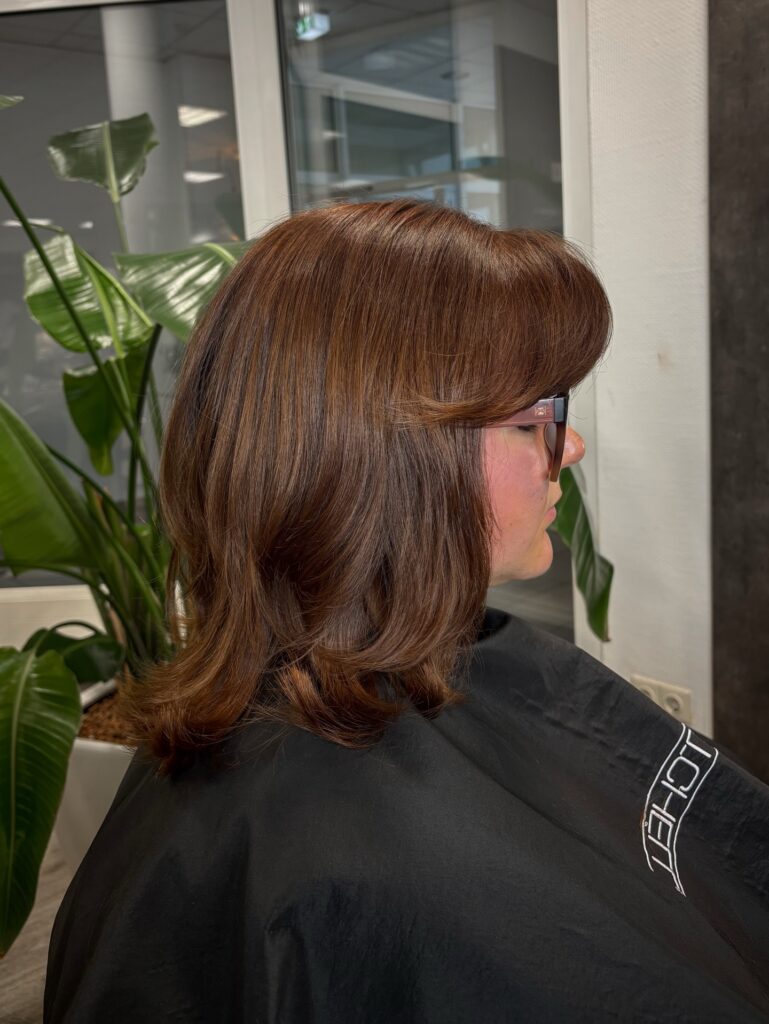 A woman in side profile wearing glasses and showcasing a jaw length choppy auburn brown bob hairstyle with a side fringe and outward flicked layers.