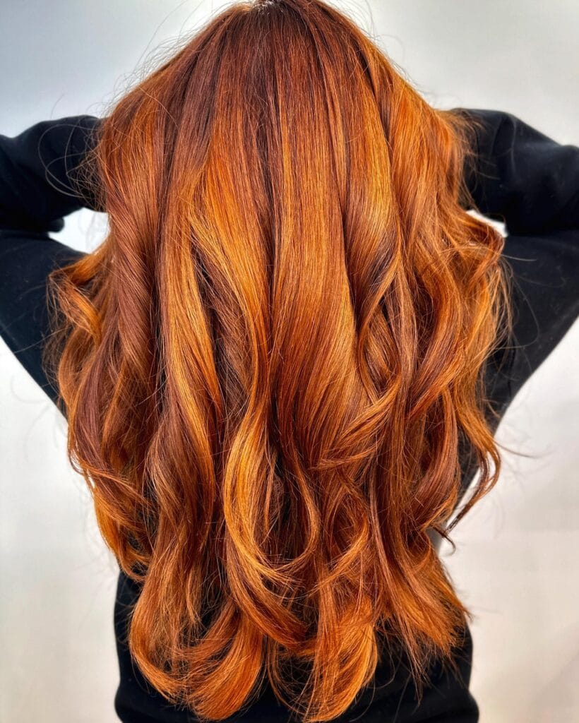Long layered haircut with loose flowing waves and vibrant copper-red color, styled with soft movement and natural volume for a rich, dimensional look.