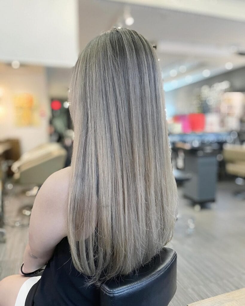 Long straight haircut with smooth layers and cool ash blonde highlights, creating a sleek, glossy look with soft blended dimension.