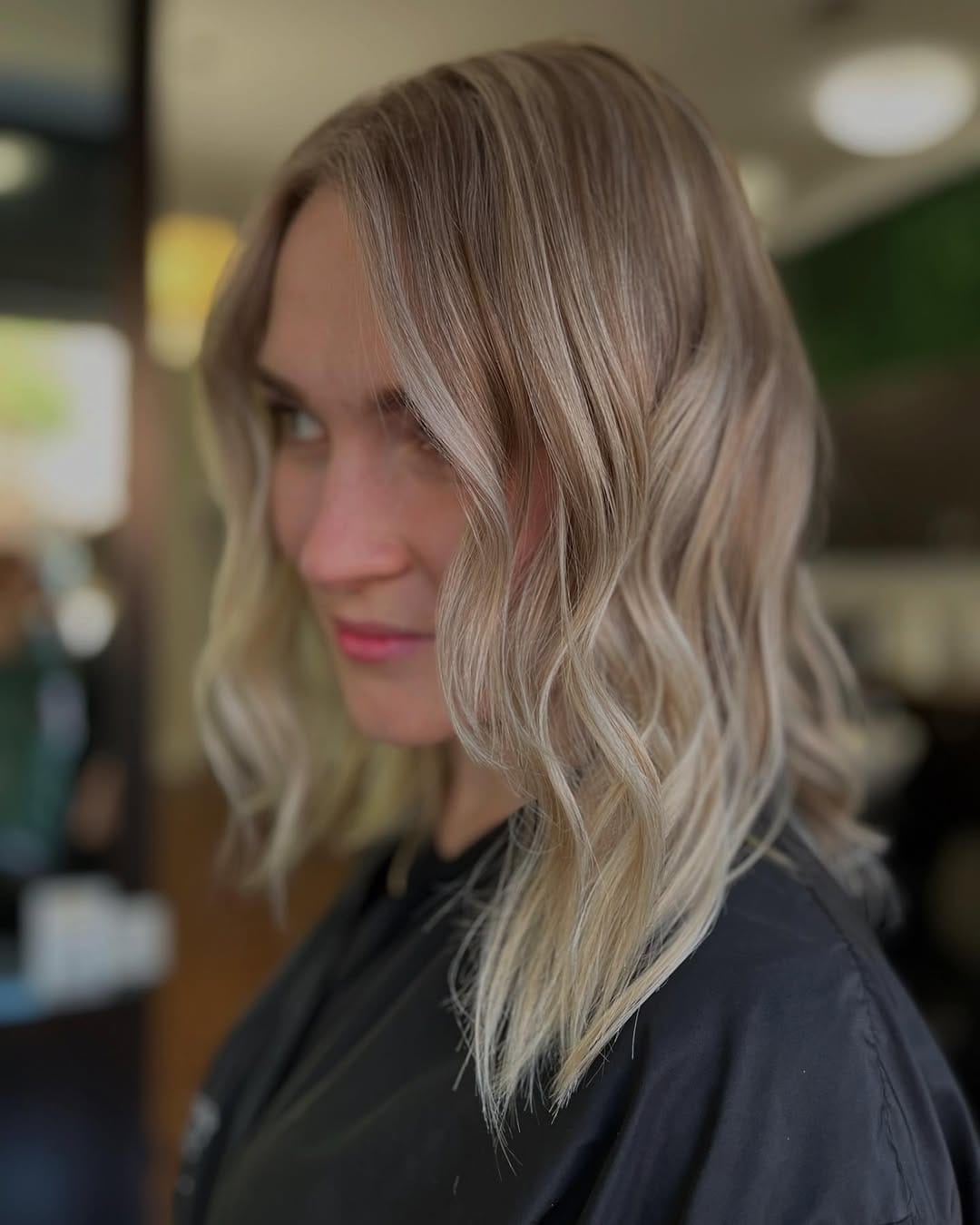 Mid-length blonde hair with a deep side part and soft, loose waves creating a smooth, dimensional look.