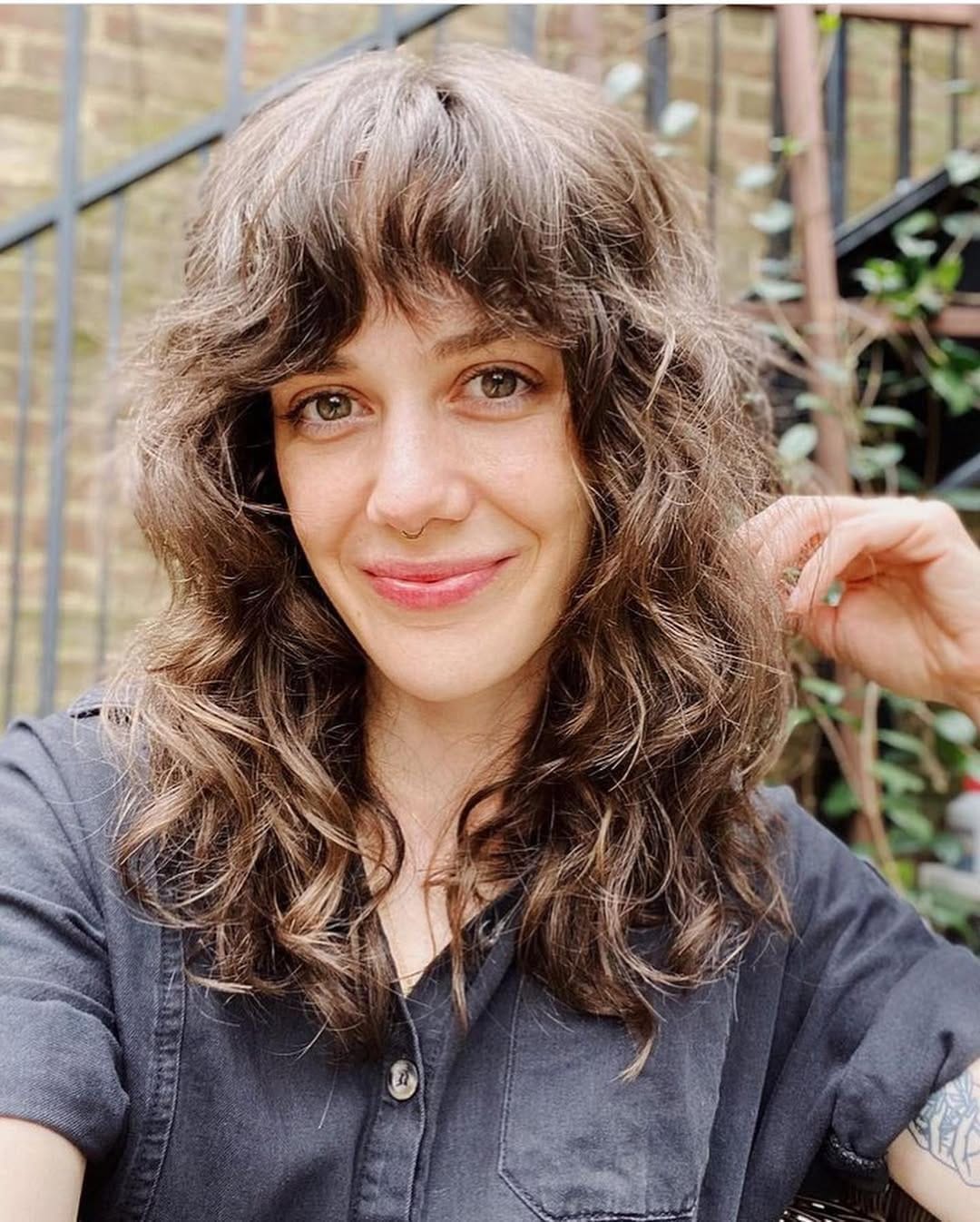 Neck-length layered shag haircut on wavy brown hair with soft bangs and natural texture for a relaxed, tousled look.