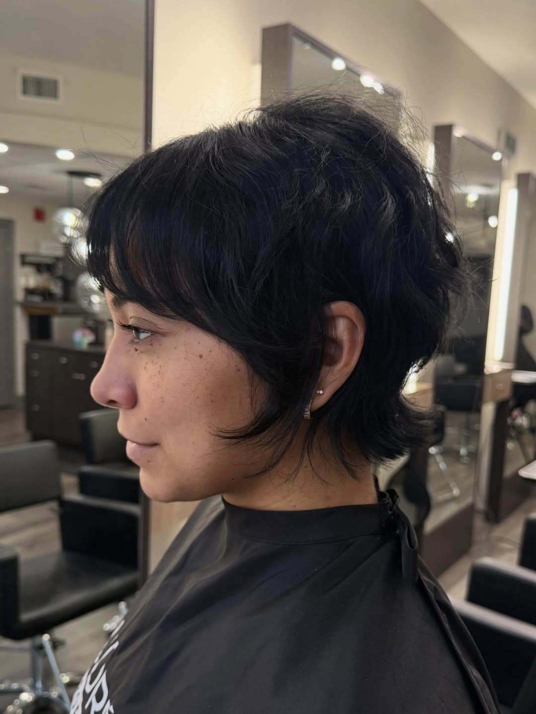 Short textured bixie haircut on dark wavy hair with soft layers, light bangs, and slightly longer pieces around the nape for a modern, tousled look.