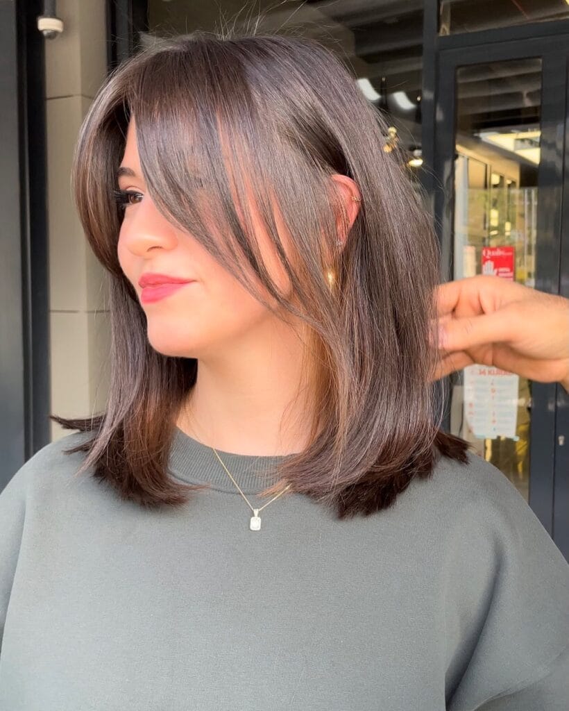 Shoulder-length layered bob with soft, smooth blowout styling and long side-swept bangs that frame the face.