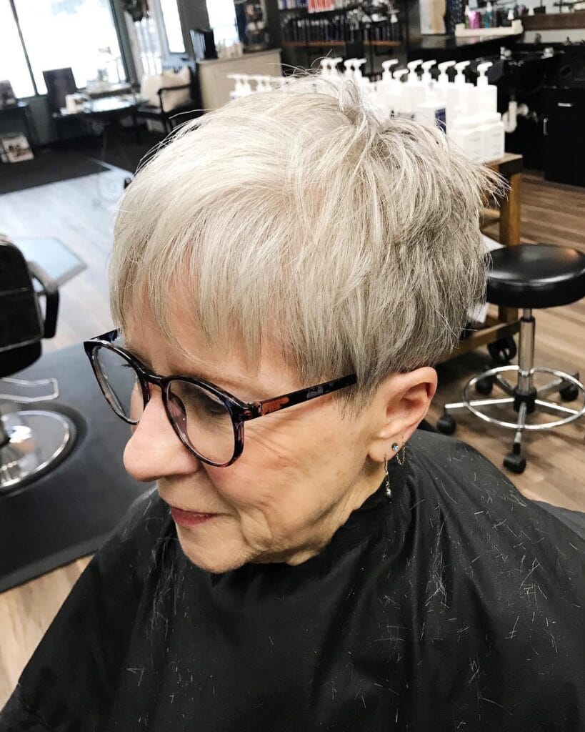 A woman with a short airy ash-silver pixie cut and delicate wispy bangs wearing dark-rimmed glasses.
