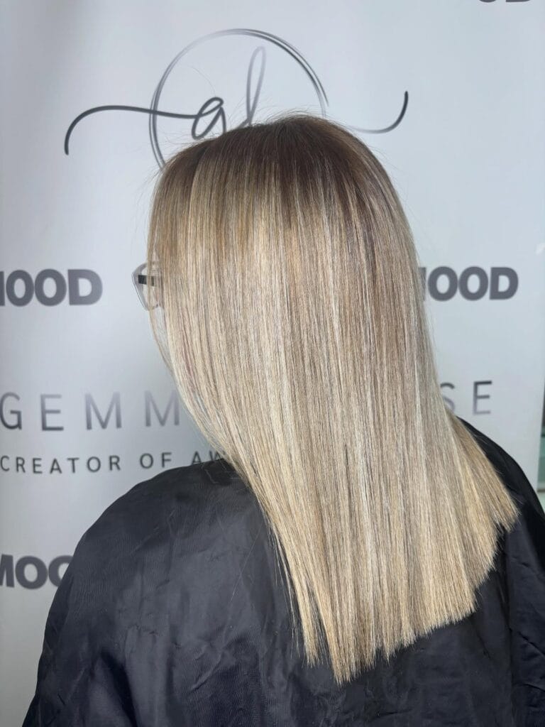 A woman with shoulder-length, straight, icy blonde hair featuring dark shadow roots and a blunt-cut hemline.
