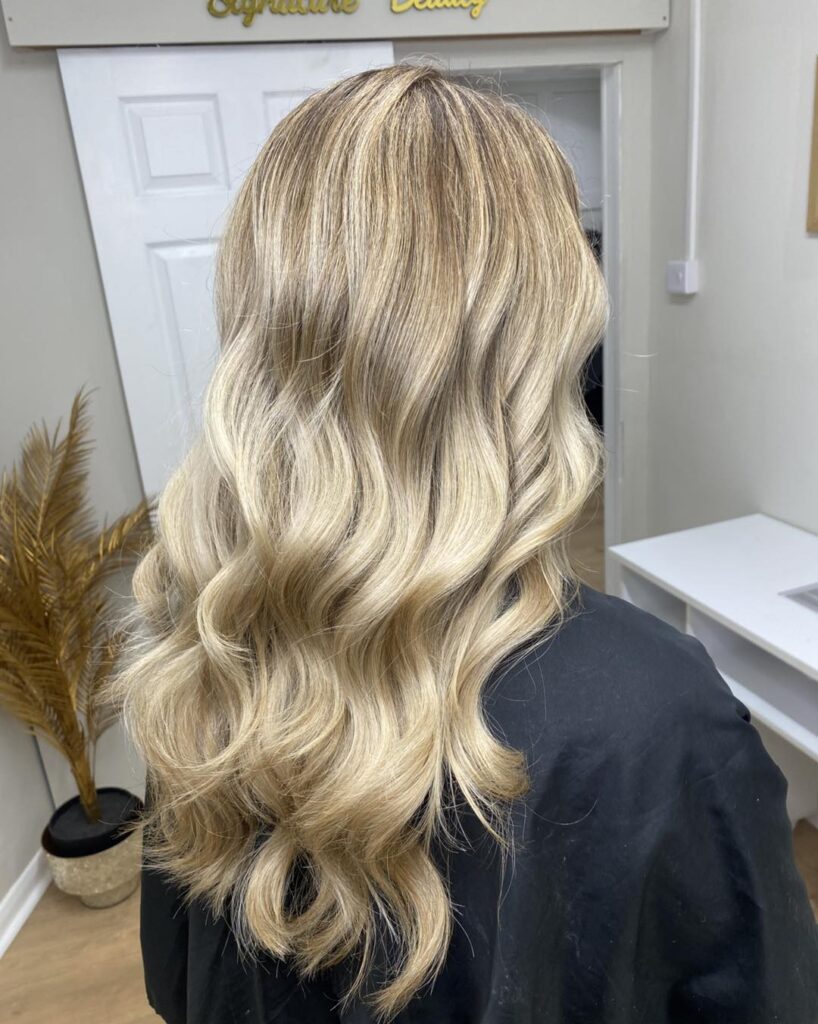 A woman with medium length ash blonde hair styled in smooth uniform waves with dimensional cool toned highlights.