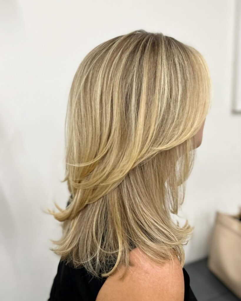 A side view of a woman with medium length butter blonde hair featuring dramatic feathered layers and flicked out ends.
