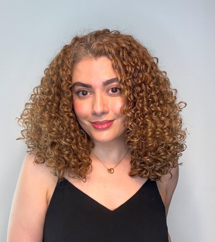 A woman with shoulder length caramel brown hair featuring very defined and uniform tight curls.