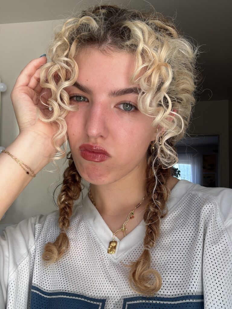 A woman with two brunette braids and bright blonde curly tendrils framing her face.