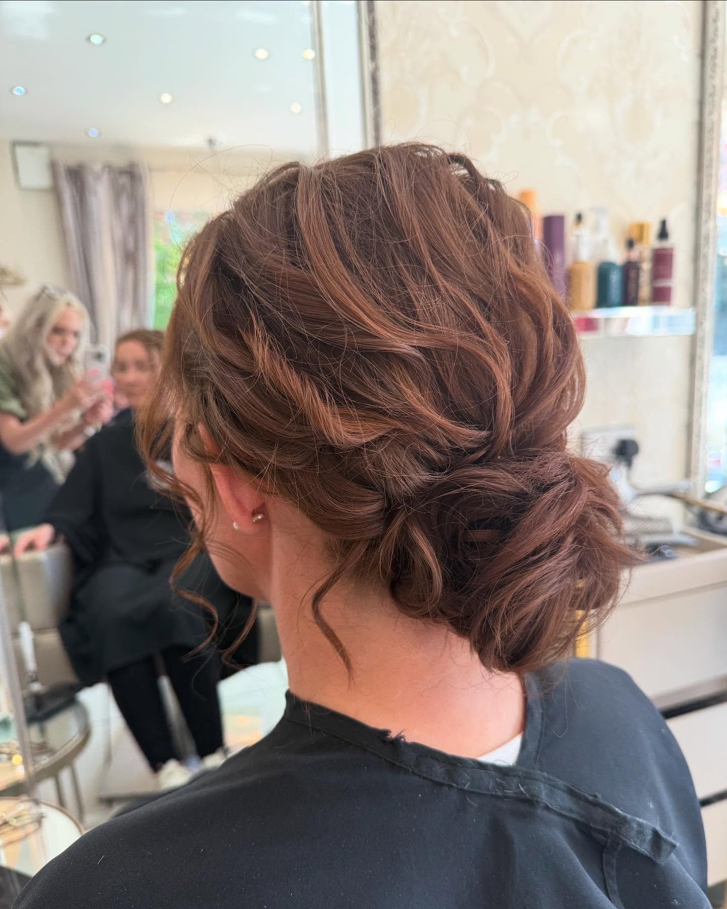 A back view of a woman with auburn hair styled in a textured low bun with loose braided side sections.