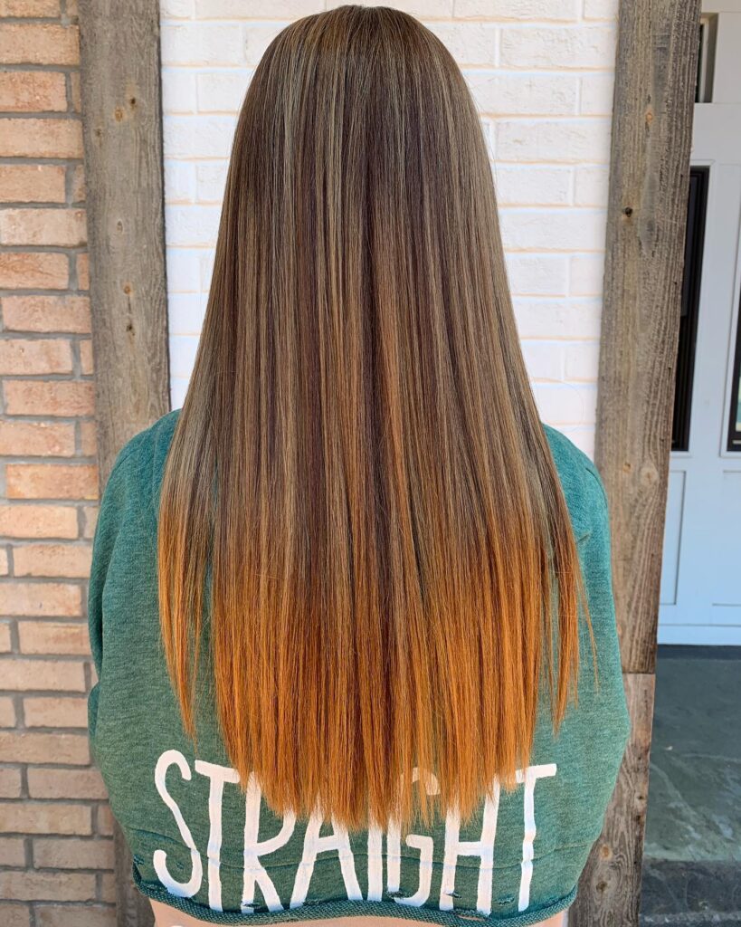The back view of a woman with very long straight hair featuring a dark brown base and bright copper orange ends.