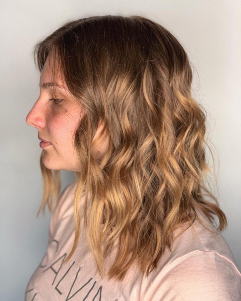 A woman with a beachy shoulder length lob featuring honey bronze highlights and messy undone waves.